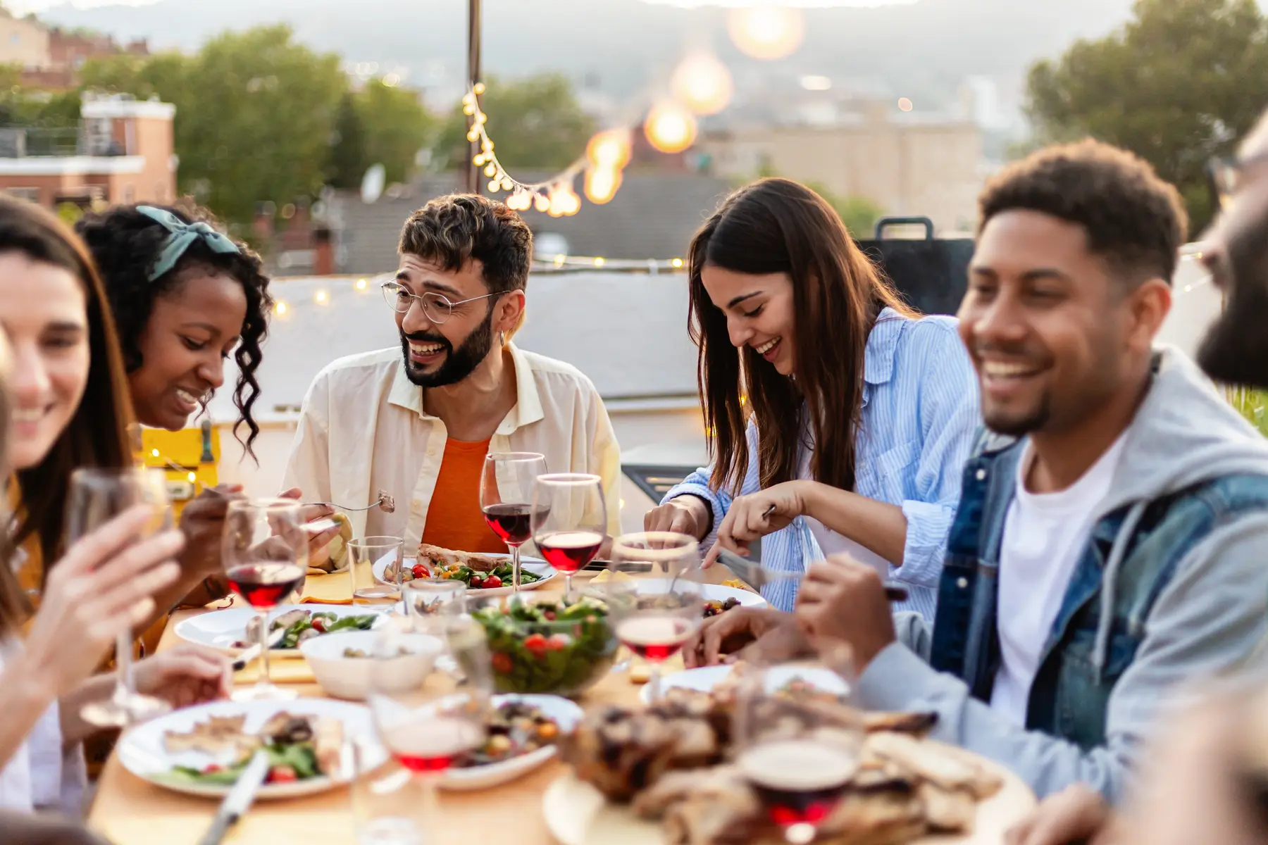 Un grupo de amigos come y ríe en una terraza al atardecer